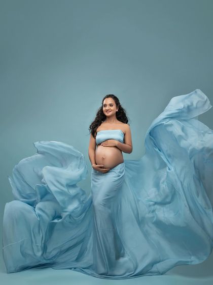 A smiling portrait in the flowing blue gown. The fabric toss creates a sense of joy and celebration around the mother-to-be.