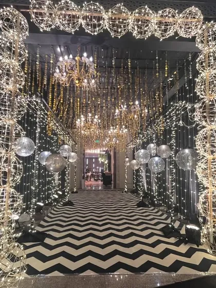 I make sure your guests are wowed from the moment they arrive. This glamorous Sangeet night entrance features a dramatic black and white chevron walkway, illuminated by thousands of fairy lights and sparkling chandeliers, setting the tone for an unforgettable party.