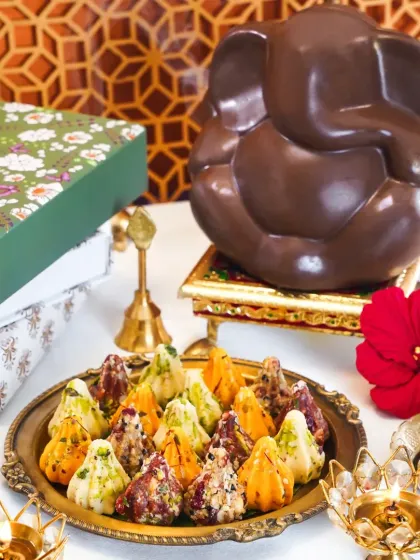 A festive spread for Ganesh Chaturthi, featuring a chocolate Ganesha idol and a platter of assorted modaks. The traditional brass diyas and flowers create a divine and celebratory atmosphere.