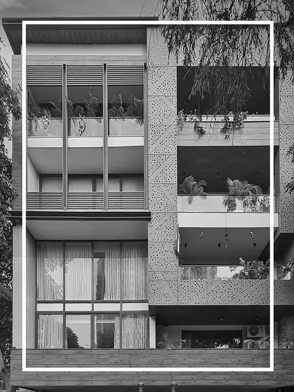 A black and white version of a modern residential facade, emphasizing its form and texture. The design integrates functionality and aesthetics through the use of glass, perforated aluminum jali, and high-pressure laminate.