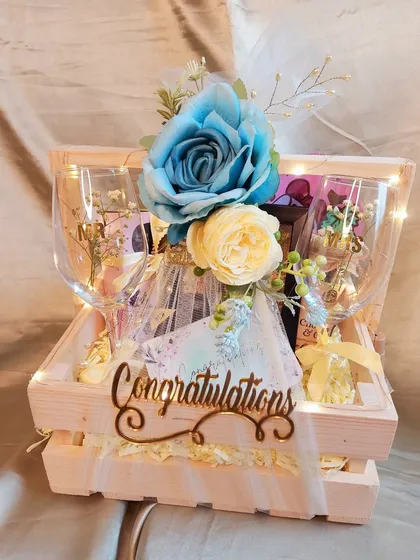 Love and happiness in a basket. This 'Congratulations' hamper for a newlywed couple features personalized wine glasses, snacks, and a beautiful blue and yellow floral theme.