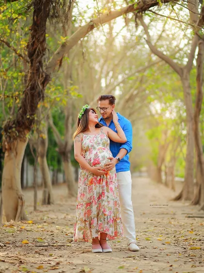 A beautiful full-length portrait of a couple on a tree-lined path. The floral dress and floral crown add a touch of bohemian charm to the outdoor setting.