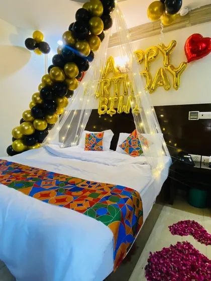 A different perspective of the black and gold birthday decor, showing the "Happy Birthday" foil balloons and rose petals scattered on the floor.