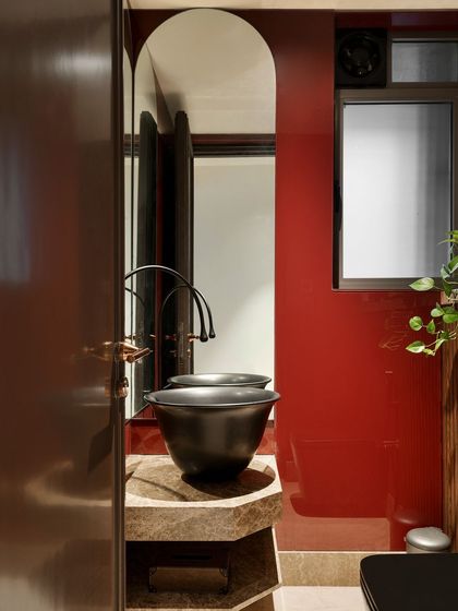 The powder room is a space of organized chaos. A bold red wall provides a vibrant backdrop for a unique black basin set on a stone pedestal, creating a memorable experience for guests.