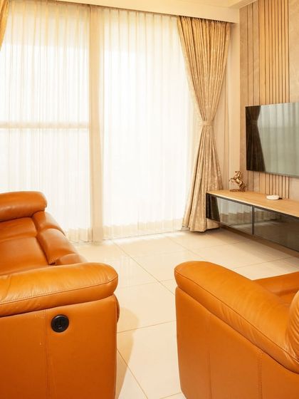 The living room at Brigade Cornerstone Utopia, featuring a comfortable tan leather recliner sofa and a simple TV unit with vertical fluting.