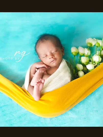 A newborn sleeps in a bright yellow hammock against a vibrant turquoise background. This shot highlights our creative use of color and props for a unique portrait.