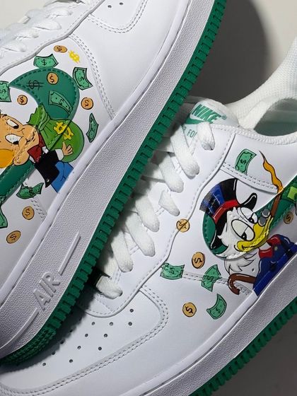 A close up of the Richie Rich and Scrooge McDuck custom Air Force 1s. The detail on the characters and the flying money is super crisp.