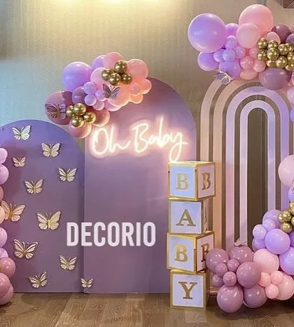 This butterfly-themed baby shower decor combines two arched backdrops for more dimension. The setup includes an 'Oh Baby' neon sign and transparent 'BABY' blocks filled with balloons, adding multiple layers of detail.