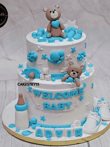 A sweet two-tier "Welcome Baby" cake. This 5kg blueberry cake is adorned with fondant baby items like shoes and a bottle, with cute teddy bears on each tier.