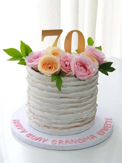 A 70th birthday cake that is both pretty and elegant. This design features delicate fondant ruffles with gold-dusted edges and is topped with fresh roses. The flavor inside was a delicious salted caramel.
