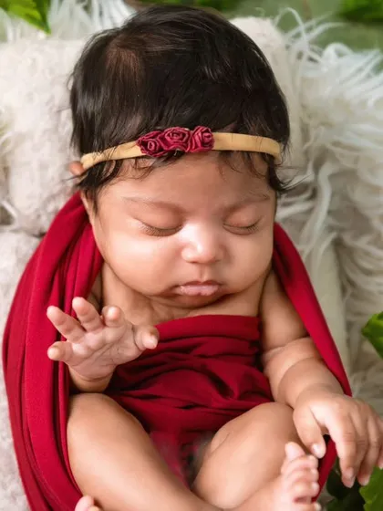 A close-up of the newborn in the red wrap and ivy setup, showing her delicate hand gestures.