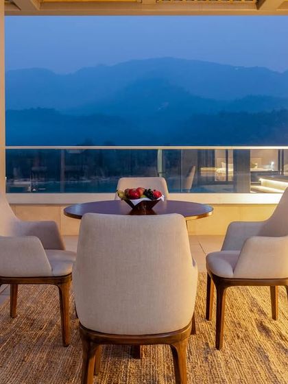 An evening view from the Modi Yoga Retreat in Rishikesh. This boutique hotel space is designed for tranquility, with a seating area that overlooks the Ganges against a backdrop of mountains, creating an elegant and peaceful atmosphere.