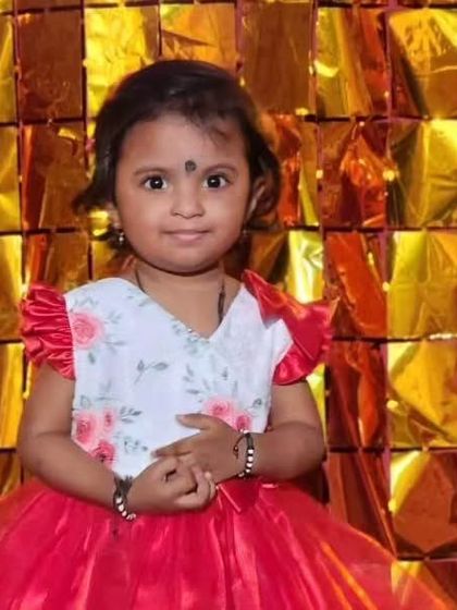 A sweet girl in a red and white floral dress against a festive gold background. Her happy expression is the best accessory.