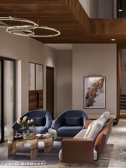 The living area is furnished with cozy fabrics, including deep blue armchairs and a tan leather sofa. Gold metal accents in the coffee table and lighting add a touch of warmth and luxury.
