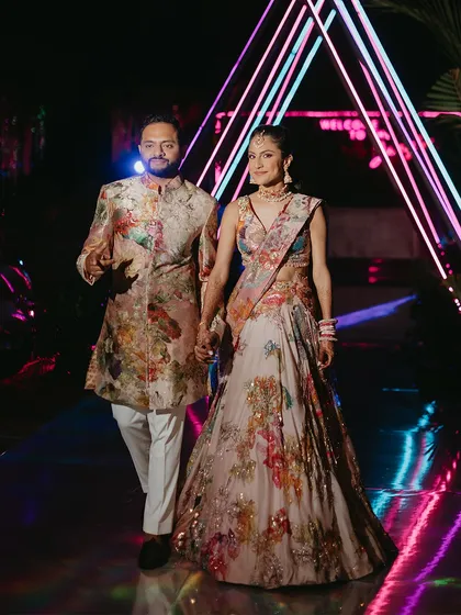 The couple makes their grand entrance at the Sangeet. The neon lights of the "Welcome to the Jungle" theme create a dramatic backdrop for their stunning floral ensembles.