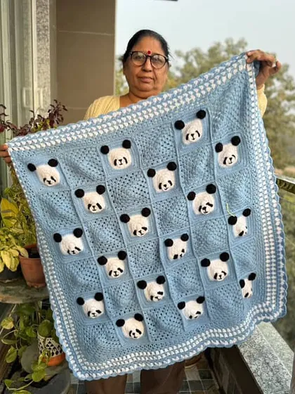 One of our talented artisans proudly displaying the finished panda baby blanket. The light blue and white color scheme is a popular choice for baby boys.