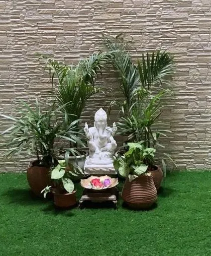 A Ganesha statue placed centrally on an artificial grass lawn, surrounded by Areca palms, creates a simple and elegant spiritual corner in this outdoor space.
