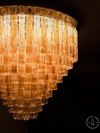 A colossal chandelier featuring tiers of fluted glass in warm amber and clear tones. Its grand scale and textured glass elements make it a stunning centerpiece, ideal for large, open spaces that require a significant and artistic lighting installation.