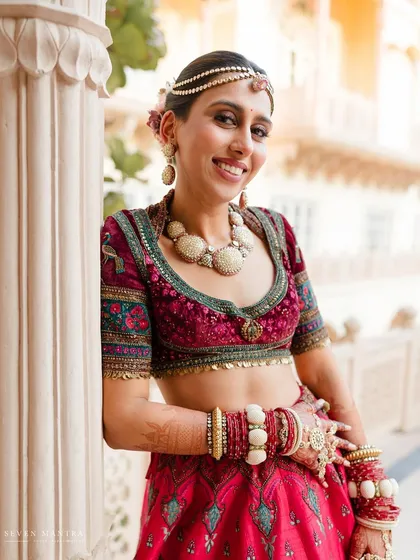 A radiant smile that lights up the frame. Leaning against a palace pillar, the bride's joy is the central focus. Her unique shell-based jewelry and vibrant lehenga were styled to feel both traditional and bohemian.