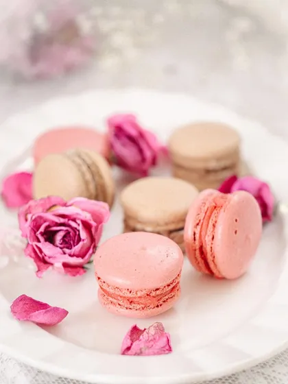 Another shot of the macarons, this time on a delicate white plate with scattered rose petals, enhancing the romantic and elegant feel.