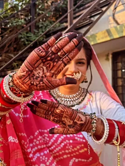 A playful pose from a bride showcasing her portrait mehndi. The design features a portrait of a deity on one hand and a traditional motif on the other.