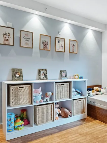 A storage solution for a kid's room, with a white shelving unit filled with woven baskets and stuffed animals. The gallery wall above adds a personal and artistic touch.