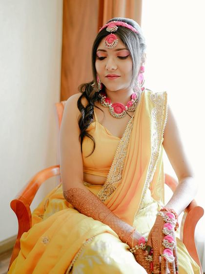 A serene moment before the Haldi festivities begin. The makeup is kept light and fresh with a pop of pink on the eyes to match her jewellery.