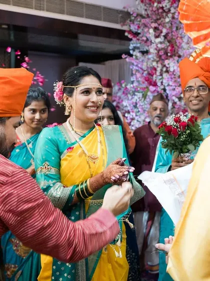 A bride smiling as she participates in a wedding ritual with her family.