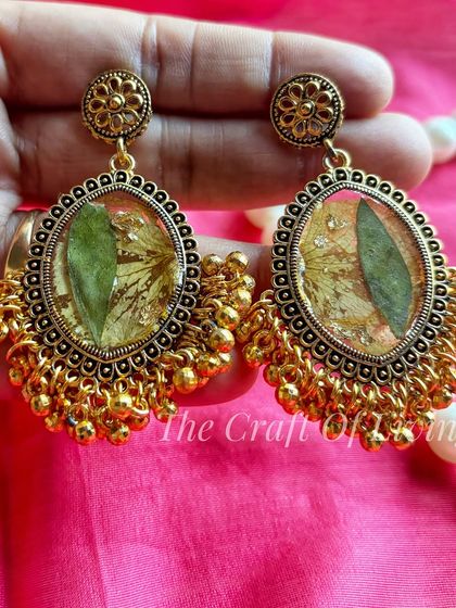 A pair of traditional gold-toned earrings with preserved green leaves inside. This shows how I can use different parts of a plant to create unique jewelry.