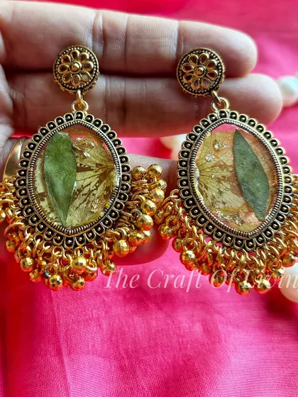 A pair of traditional gold-toned earrings with preserved green leaves inside. This shows how I can use different parts of a plant to create unique jewelry.