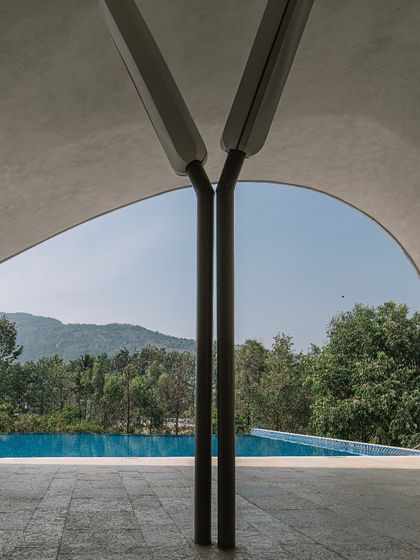 A detail of the tree-like structural columns supporting the sweeping parametric roof. This perspective highlights how the architecture frames a perfect, uninterrupted view of the pool and the lush green hills in the distance.