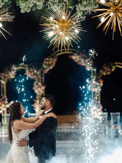 The couple shares their first dance amidst a shower of sparklers. The starburst chandeliers and floral arches in the background complete this picture-perfect romantic scene.