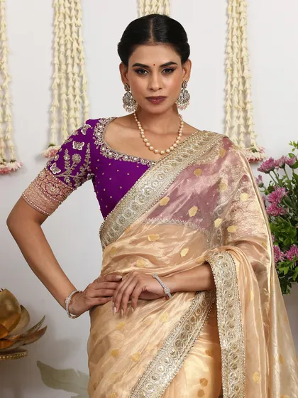 A beautiful ivory organza saree with gold polka dots, paired with a contrasting purple embroidered blouse.