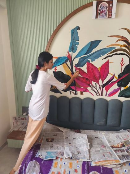 Me at work on the tropical bedroom mural, carefully painting the vibrant foliage. This shows the scale of the artwork in relation to the bed.