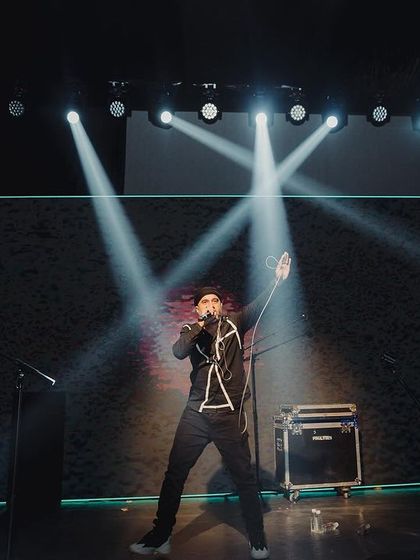 A solo performer on the dark, dramatically lit stage, creating a powerful and intimate moment during the Sangeet.