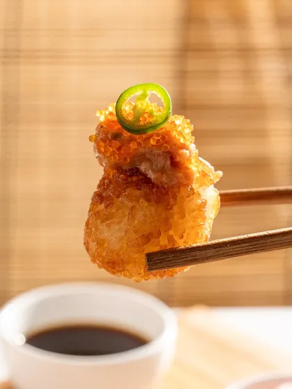 A single piece of crispy rice sushi held by chopsticks. This minimalist shot puts all the focus on the texture and toppings.