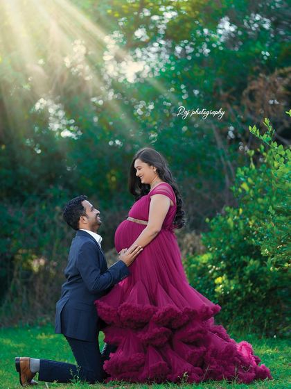 A tender moment with the father-to-be kneeling to kiss the baby bump. The mother-to-be is wearing a wine-colored ruffled gown.