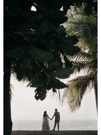 A silhouette of the couple holding hands against the backdrop of the sea and palm trees. This romantic shot captures a quiet, intimate moment during their pre-wedding shoot.