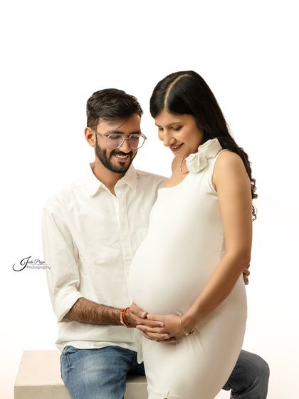 A classic couple's pose against a pure white background. They both look down at the baby bump, sharing a quiet moment of anticipation for their little one's arrival.