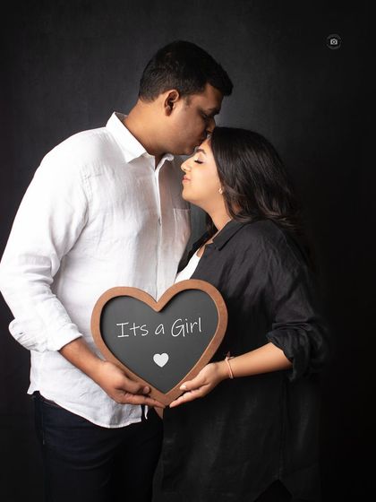 A tender moment as a partner kisses his wife's forehead while they hold an "It's a Girl" sign. A perfect combination of intimacy and announcement.