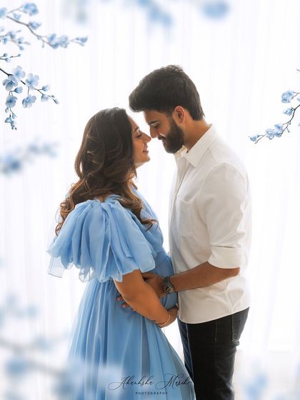 A soft and dreamy maternity portrait. The flowing blue gown and delicate floral accents create a serene and romantic atmosphere for the expecting couple.