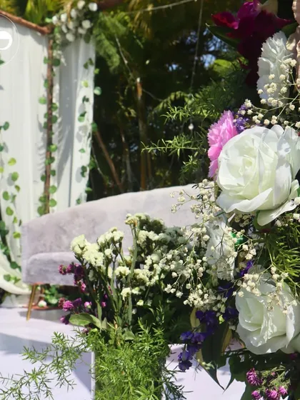 A close-up of the floral decor for an outdoor Roka. The arrangement of white roses, pink carnations, and greenery perfectly complements the natural, sunlit setting.