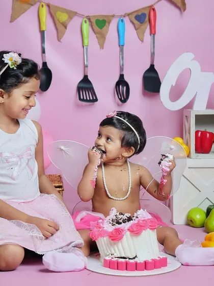 A sweet moment between sisters during a first birthday cake smash. Big sister watches on as the birthday girl enjoys her cake.