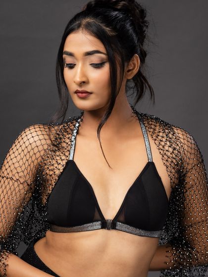 A model wearing a black bralette with silver straps and a sparkling mesh shrug. This is a great example of a modern lingerie or festival-wear look.