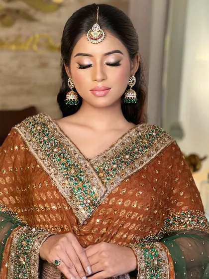 An eyes-closed shot that highlights the soft, neutral makeup and the traditional design of the earrings and tikka.