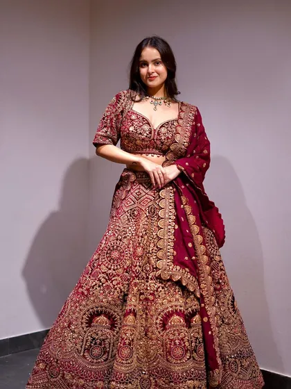 A stunning bridal lehenga in a deep maroon velvet, covered in luxurious hand-embellished details. This piece is pure opulence, perfect for a grand wedding ceremony.