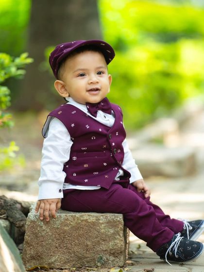 A stylish little gentleman posing on a rock. The vibrant green background of the park makes his smart outfit pop.