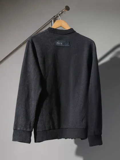 A minimalist shot of a black sweatshirt hanging on a rack against a moody, grey studio background. This style emphasizes the garment's shape and texture.