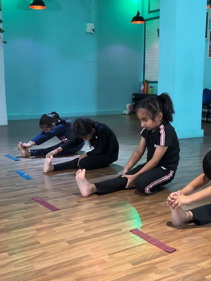 Students practice their seated stretches, each at their own pace but together as a group. We use markers on the floor to help them track their progress.