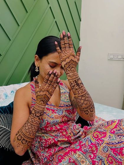 A classic bridal pose by Sneha, her hands hiding her face, drawing all attention to the intricate mehendi.